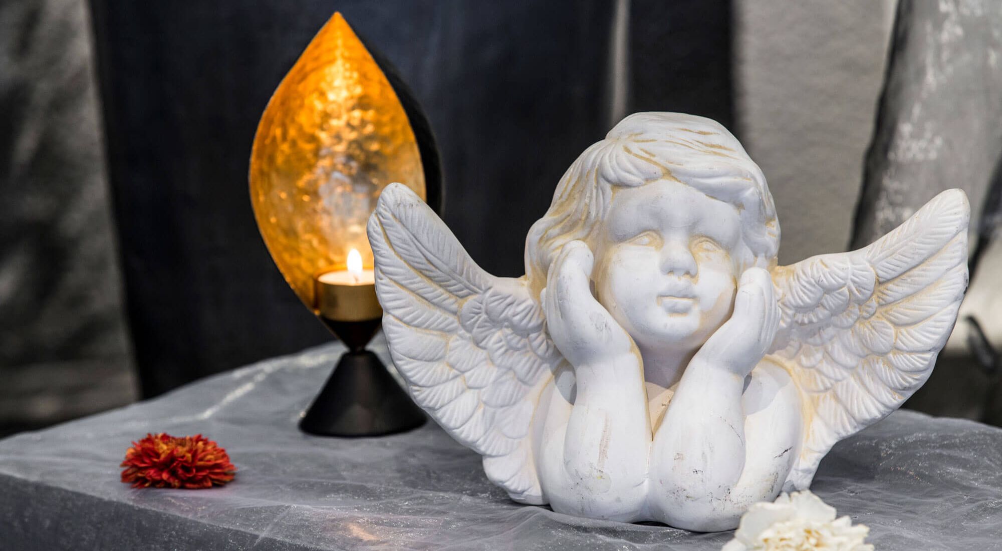 Brennendes Teelicht und ein weißer Engel auf einem Tisch